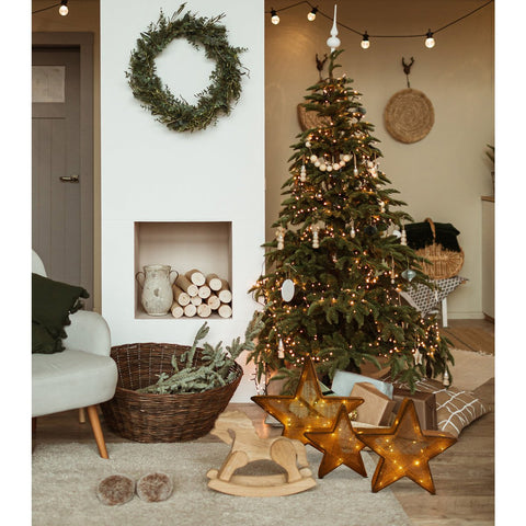 Set di tre stelle decorative a LED in tessuto e metallo marrone di varie dimensioni appoggiate sul pavimento in parquet di un soggiorno moderno in stile Japandi con l'albero di Natale