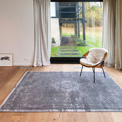 Tappeto flatweave in ciniglia e lana grigio pietra con medaglione centrale e finitura vintage sfumata Medallion Stone di Louis De Poortere steso su un pavimento in legno
