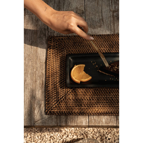 Tovaglietta rettangolare in rattan intrecciato marrone naturale Colonial disposta su un tavolo da pranzo in legno con un piatto in ceramica appoggiato sopra
