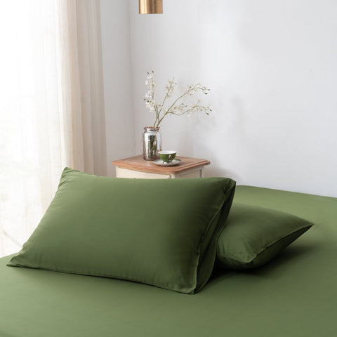A set of two pillowcases made of 100% Deep Moss green Boomba Bamboo® bamboo fabric, placed on a matching bed in a well-lit bedroom