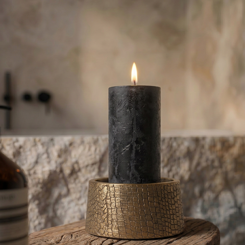 Brass candleholder with a crocodile-skin texture and a central glass stem, "The Croco" (14x22 cm), placed on a small wooden table with a lit candle