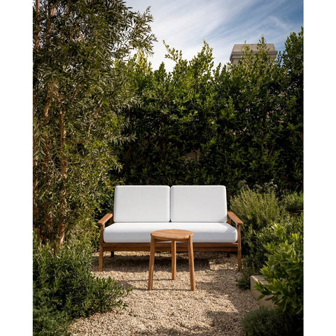 Tavolino da esterno in legno massello di teak naturale Gilimanuk di dimensioni 47x47 cm posizionato accanto a una poltrona da giardino su un terrazzo in pietra in stile Japandi