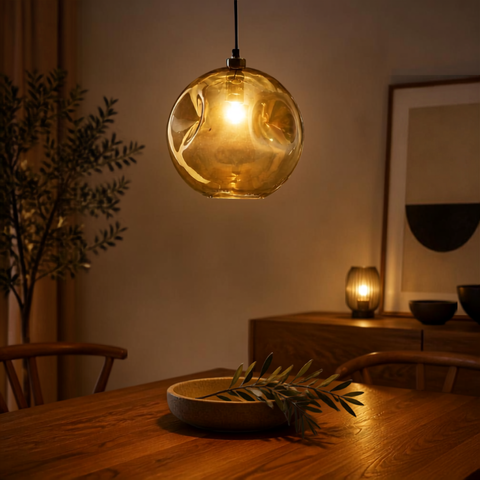 Lampada a sospensione in vetro riciclato oro pallido Bubbella 29 cm accesa sopra un tavolo da pranzo in legno massello con atmosfera ambrata soffusa
