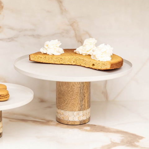 Piatto per torta rialzato bianco e legno utilizzato per servire una torta fatta in casa su una tavola in stile nordico.