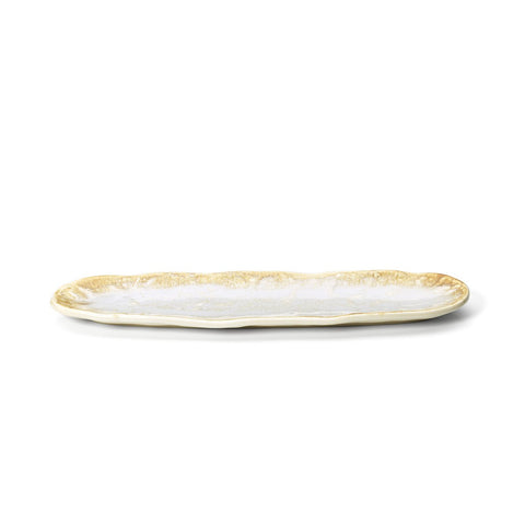 Piatto ovale allungato da portata in ceramica beige e miele bianco Da Rocha posizionato su un tavolo da pranzo in legno con preparazioni di sushi e verdure arrostite in stile Japandi