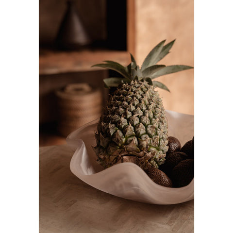 Portafrutta scultoreo in resina organica marmorizzata rosa e bianco avorio Ø 30 cm con frutta fresca al centro di un tavolo da pranzo moderno