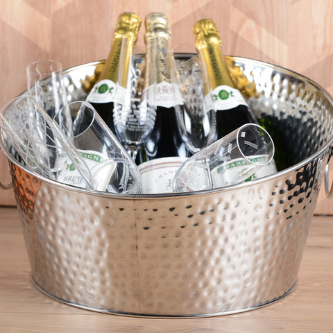 Grande secchiello da champagne in acciaio martellato lucido con ghiaccio e bottiglie posizionato su un tavolo da buffet