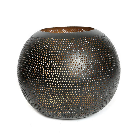 Portacandele sferico grande in ottone traforato oro nero Pierced Ball XL acceso posizionato su un tavolino basso in legno