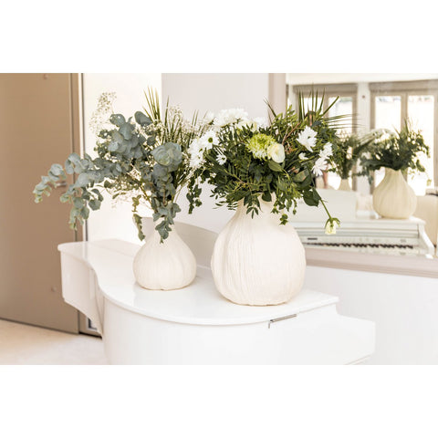 Vaso in ceramica bianco cremosico Mousse L posizionato su una credenza in legno con rami fioriti.