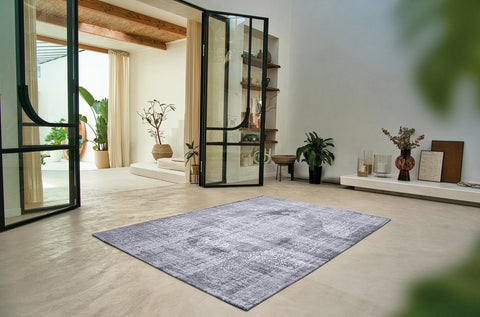 Tappeto flatweave ecologico nei toni del grigio quarzo con motivo persiano decostruito Kirman Quarzo di Louis De Poortere steso in un soggiorno Japandi con pavimento in legno chiaro e divano neutro